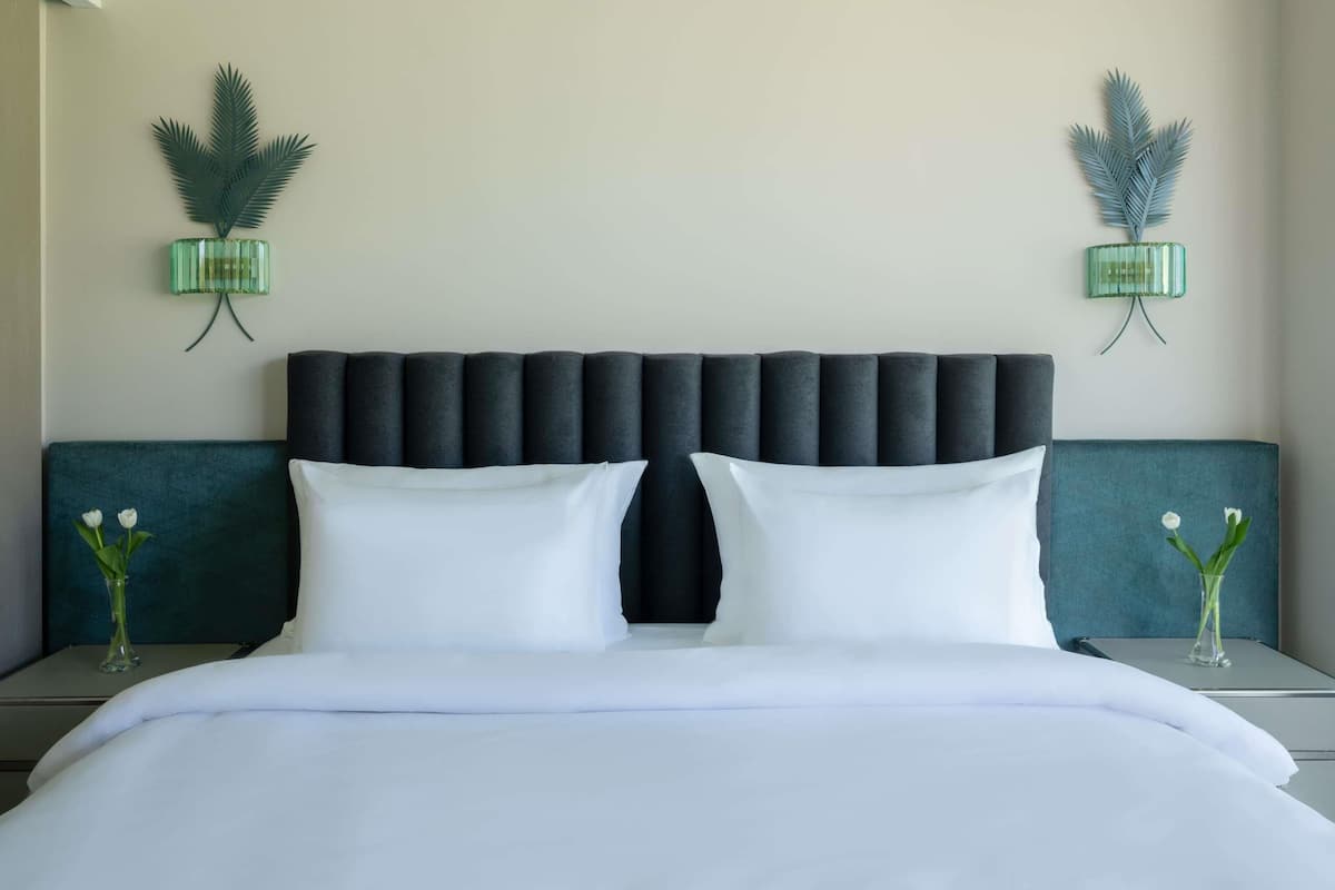 A hotel room with a large bed, two nightstands, a dark upholstered headboard, and decorative wall sconces.