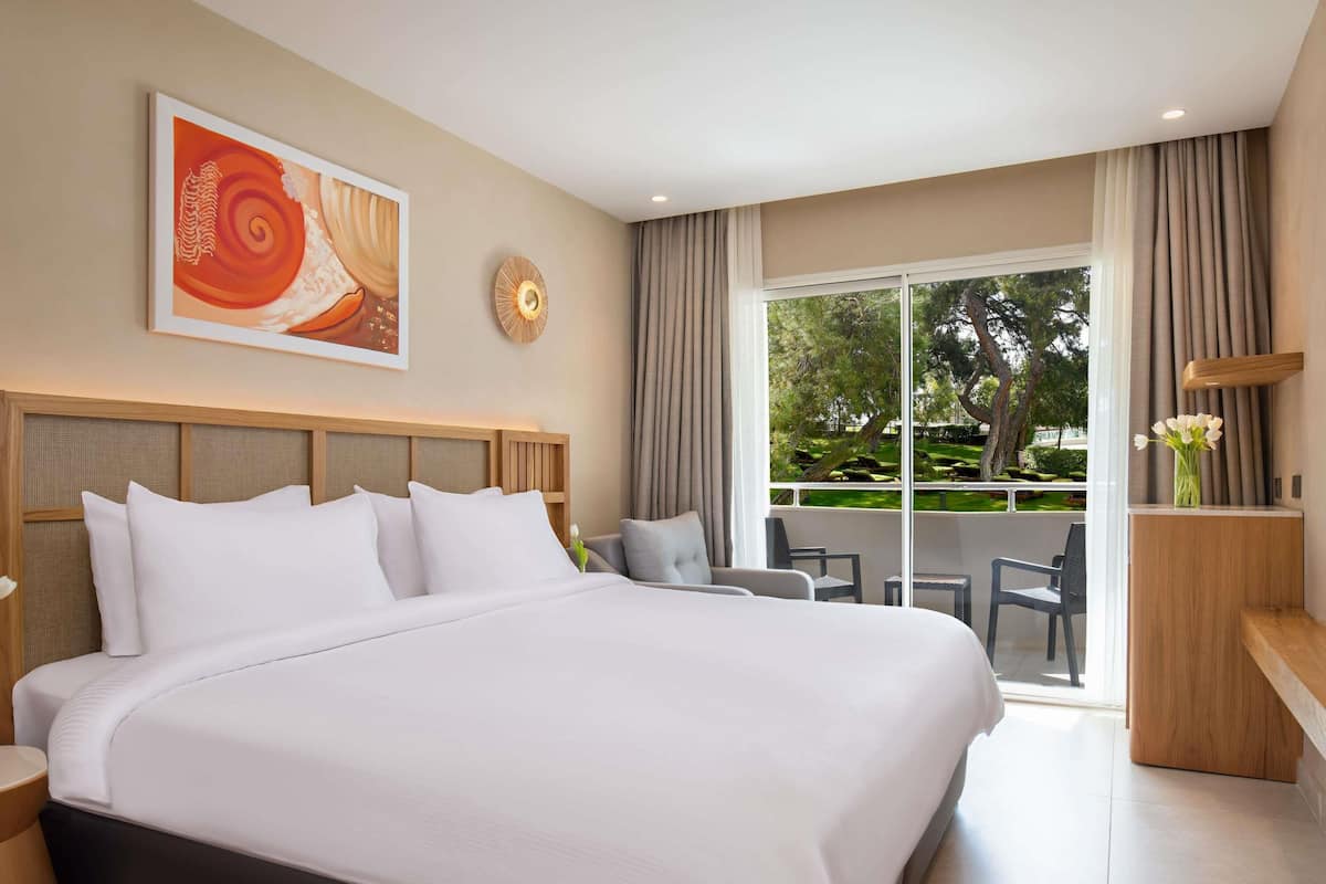 A hotel room with a large bed, a desk, a chair, a dining table, and a view of the outdoors.
