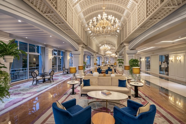 A spacious lobby with a high ceiling, chandeliers, seating areas, and large windows.