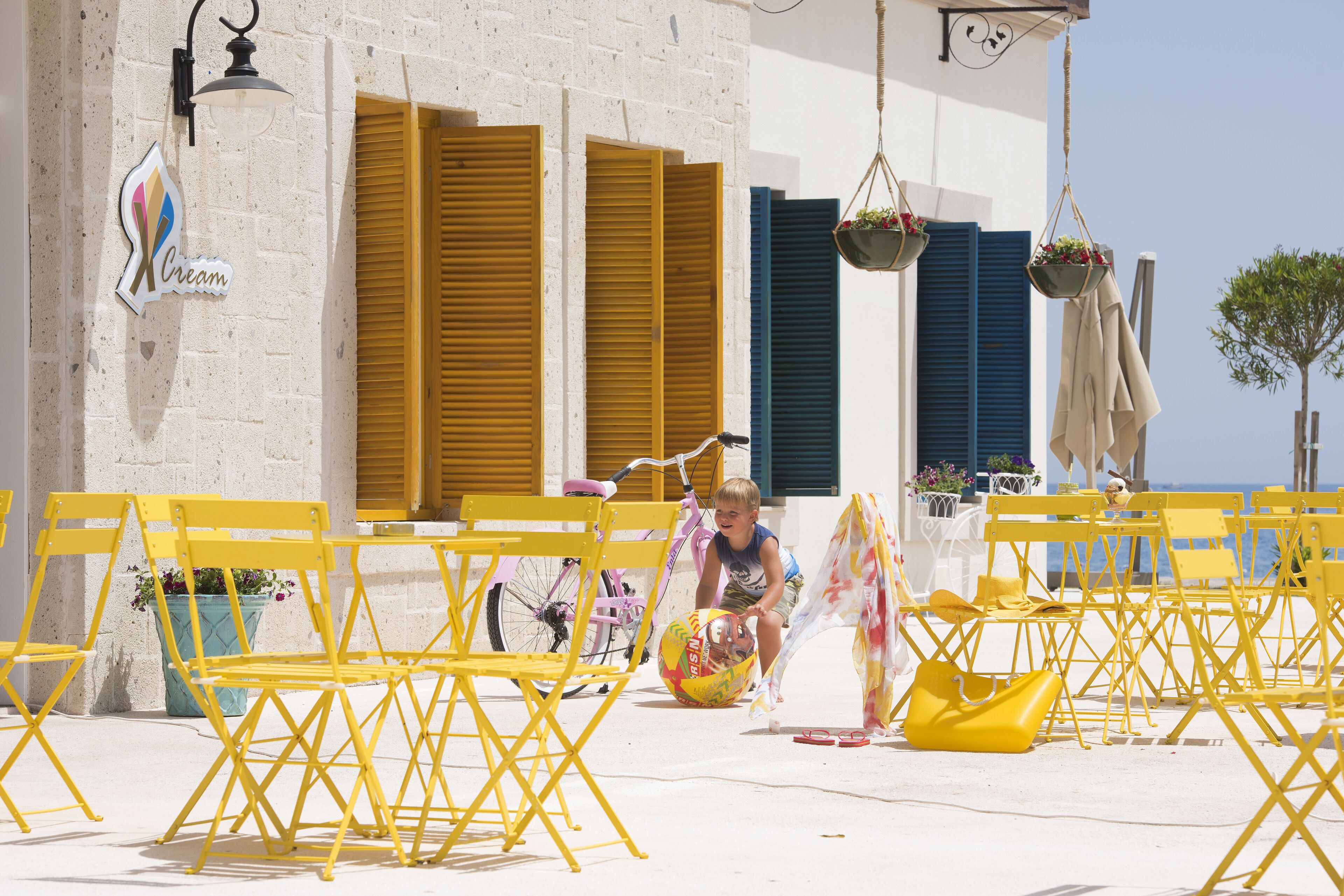 Yellow folding chairs, a beach ball, and a child playing near a building with a sign that reads "Cream".