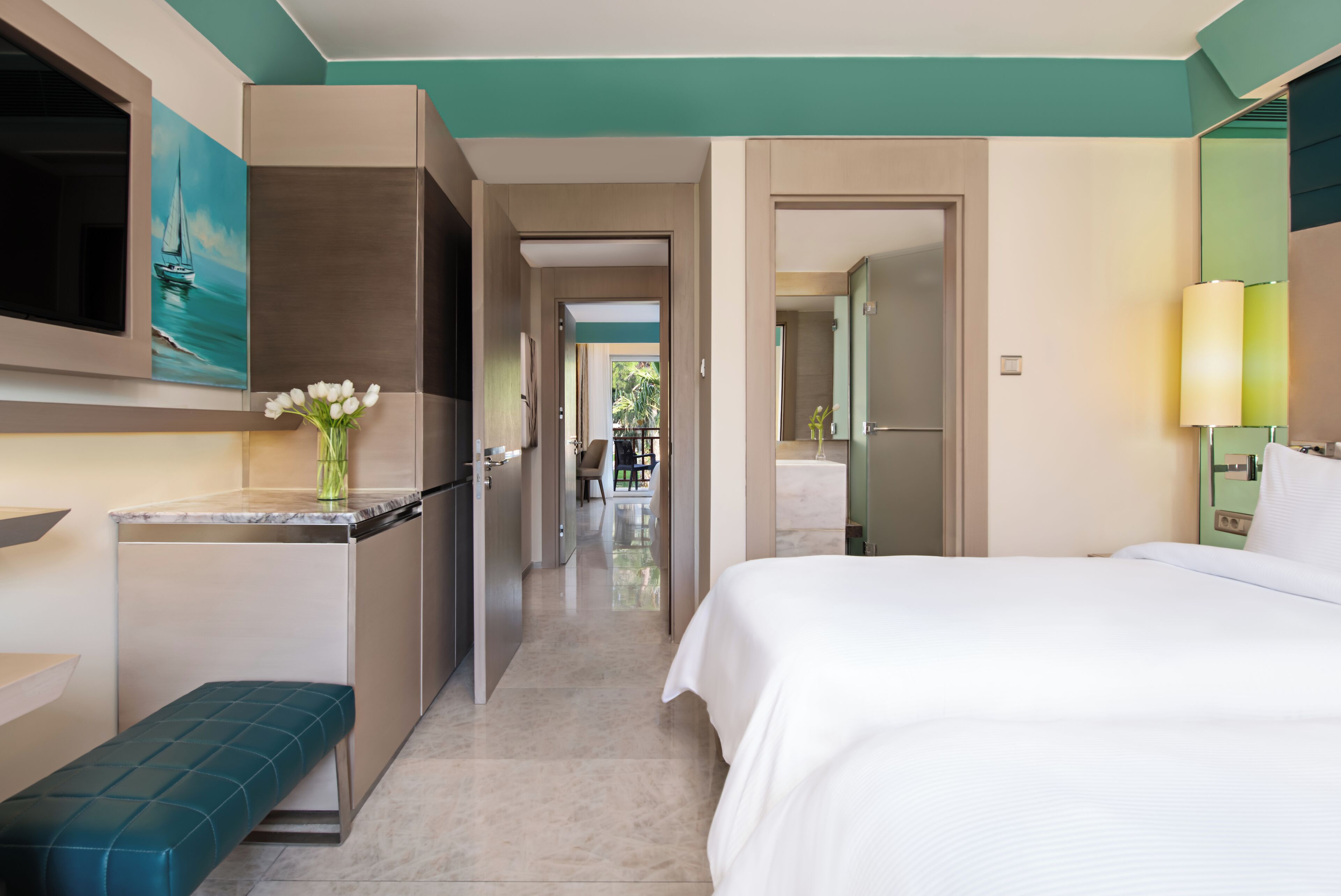 A hotel room with a bed, a bench, a small kitchenette, and a bathroom.