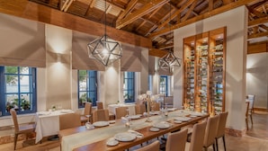 A dining area with a long wooden table set for a meal, surrounded by chairs, with a wine rack and pendant lights above. - Rixos Premium Tekirova - The Land of Legends (Kemer)