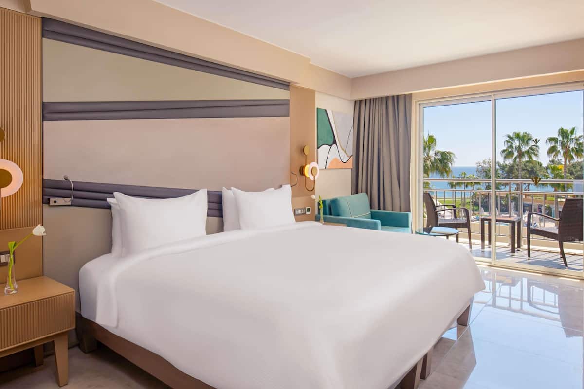 A hotel room with a large bed, a small table, a chair, a nightstand, and a view of the ocean.