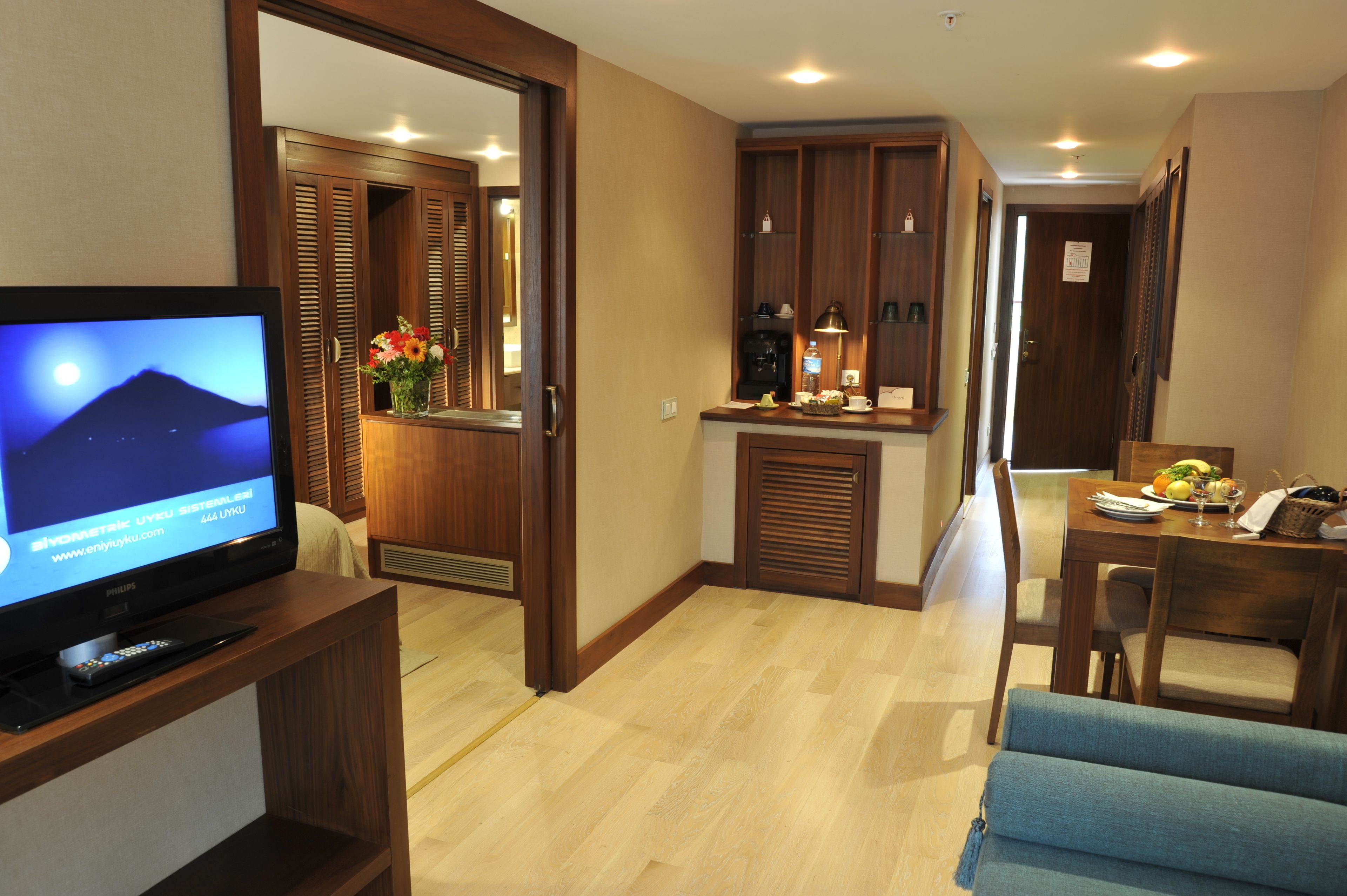 A hotel room with a television, wooden furniture, a dining area, and a kitchen.