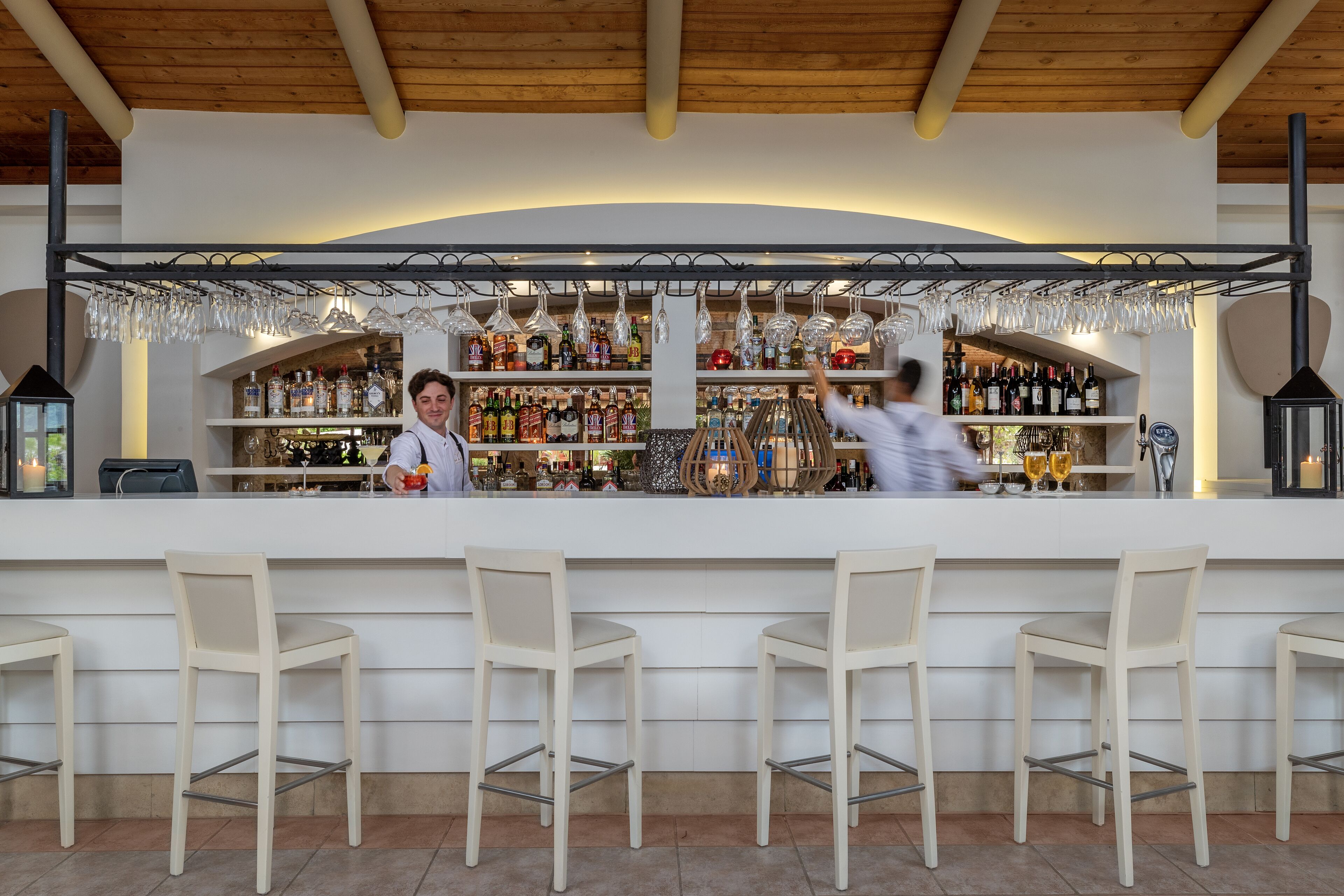 A bar area with a wooden ceiling, shelves of liquor bottles, and hanging wine glasses.