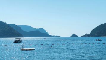 A calm sea with boats and buoys, surrounded by hills.