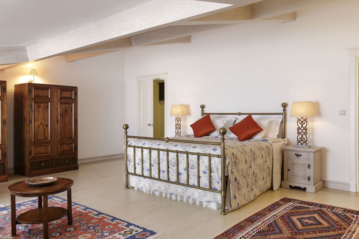 Quarto com cama, mesas de cabeceira, guarda-roupa de madeira e tapete estampado.