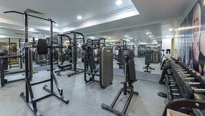 Une salle de sport équipée de divers appareils d’exercice, de miroirs et d’un mur orné d’une grande affiche.