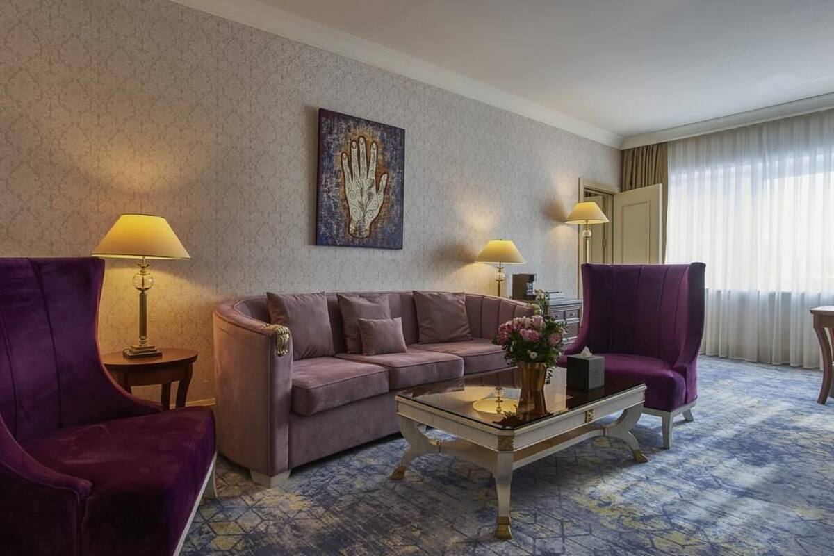 Hotellihuone, jossa on violetti sohva, lasinen sohvapöytä ja kaksi lamppua.