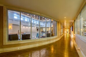 A corridor with large windows, a tiled floor, and a view of an indoor swimming pool area. - Rixos President Astana (Astana)