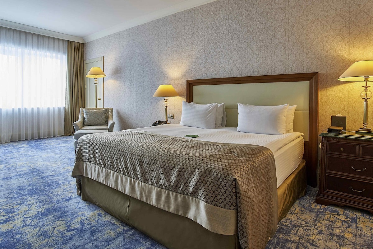A hotel room with a large bed, two bedside lamps, a chair, and a nightstand.
