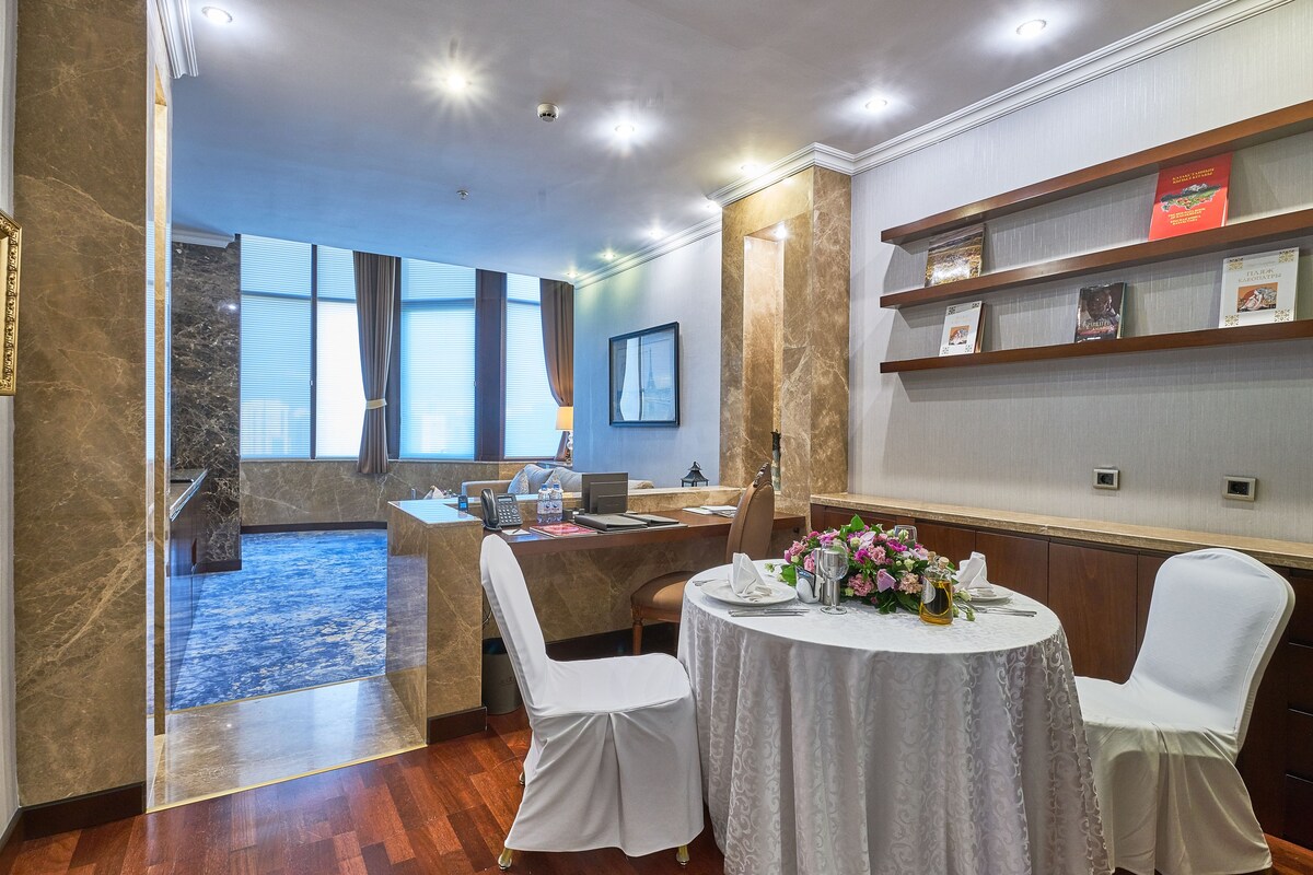 A hotel room with a marble reception desk, a round dining table with white chairs, and a blue carpeted area.