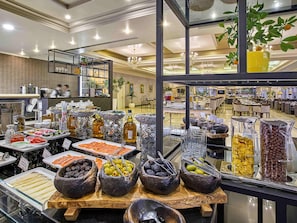 Un bufé con diferentes alimentos y bebidas, una araña y vistas del interior del hotel.