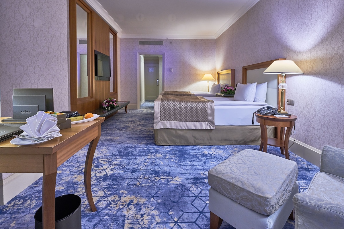 A hotel room with two beds, a desk with a telephone, a lamp, and a TV.