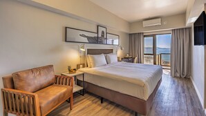 A hotel room with a bed, a wooden chair, a nightstand, a lamp, and a large window with a view. - B&B Hotels Rio Copacabana Posto 5 (Rio de Janeiro)