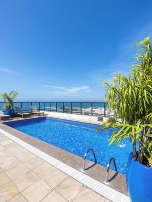 A rooftop pool with clear blue water, a view of the ocean, and a few lounge chairs.