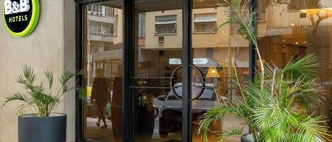 A hotel entrance with a large glass door, potted plants, and a sign reading "B&B HOTELS".