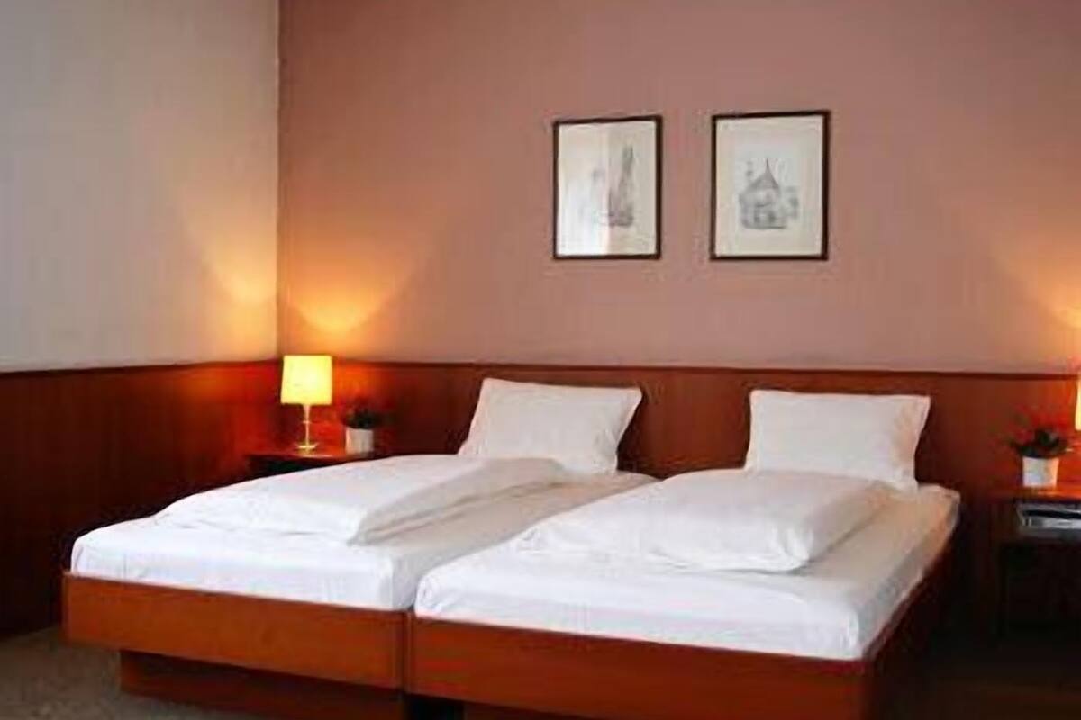Habitación de hotel con cama doble, dos mesitas de noche, una lámpara y dos cuadros en la pared.