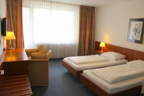 A hotel room with two single beds, a desk with a chair, a nightstand with a lamp, and a large window with curtains. - Hotel Acon (Düsseldorf)