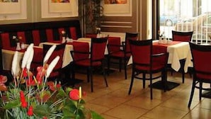L’intérieur d’un restaurant présente des banquettes rouges recouvertes de tissu, des nappes blanches et des œuvres d’art encadrées accrochées aux murs.