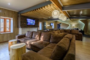 A modern living room with a large sectional sofa, wooden accents, and a stone wall. - Kiara Lodge (Clarens)