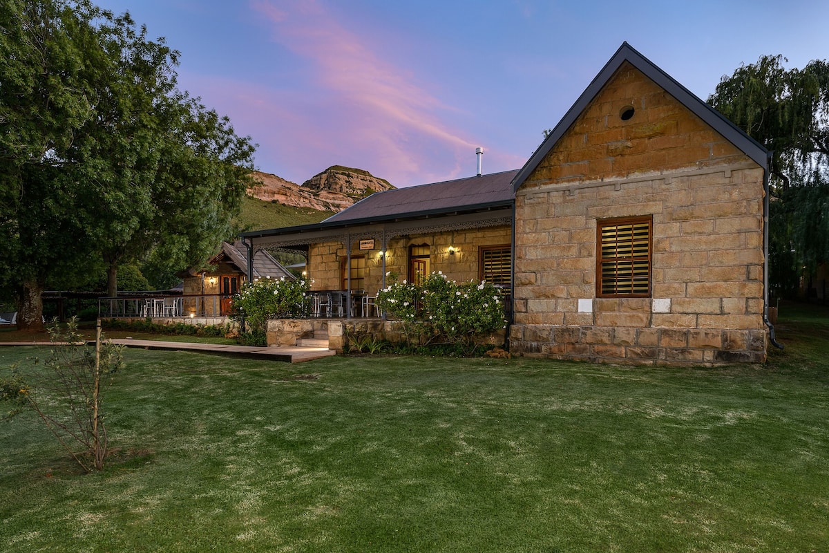 A stone building with a sloped roof, a porch with outdoor seating, and a well-maintained lawn.