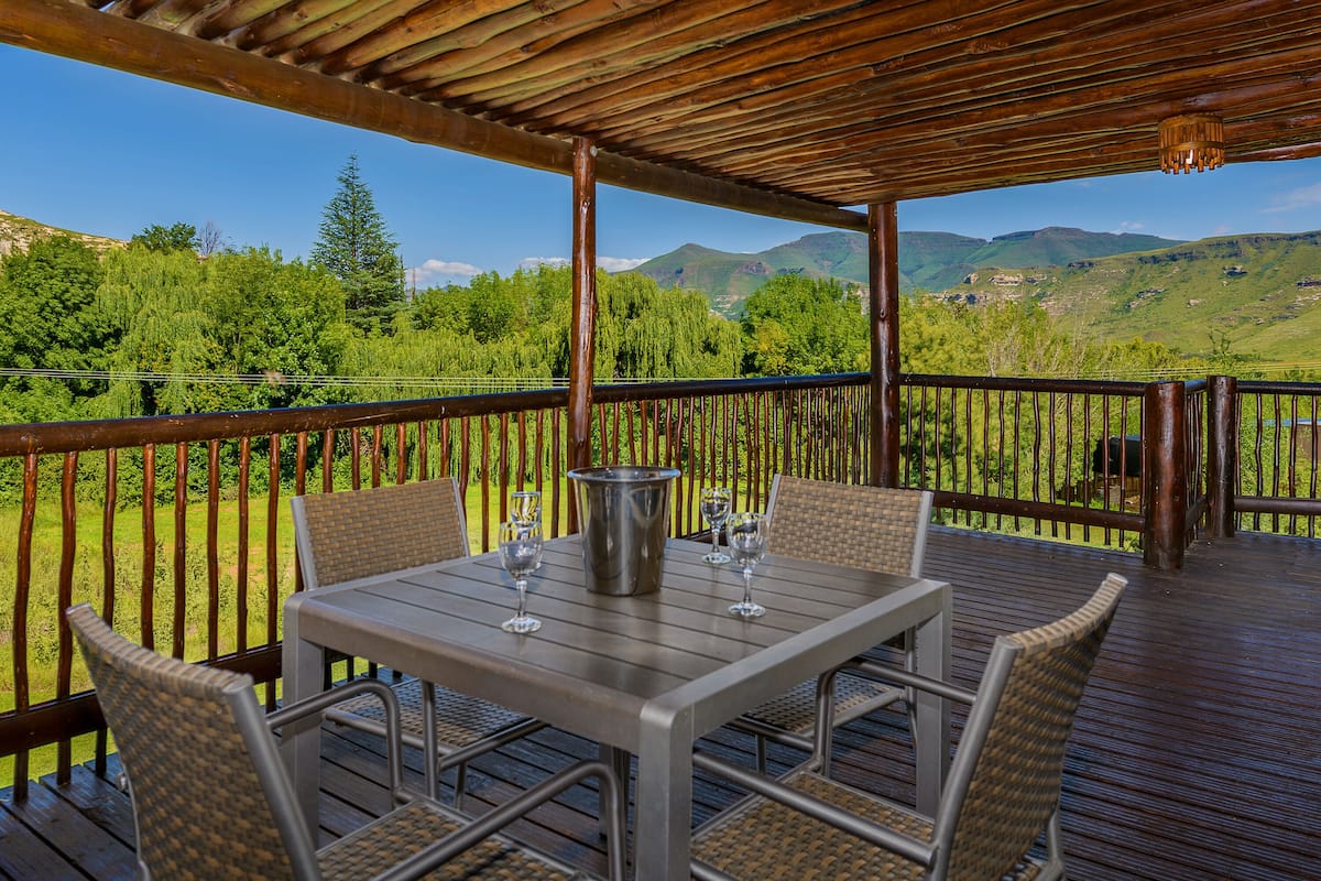 A covered outdoor seating area with a table and chairs, overlooking a lush landscape with trees and mountains.