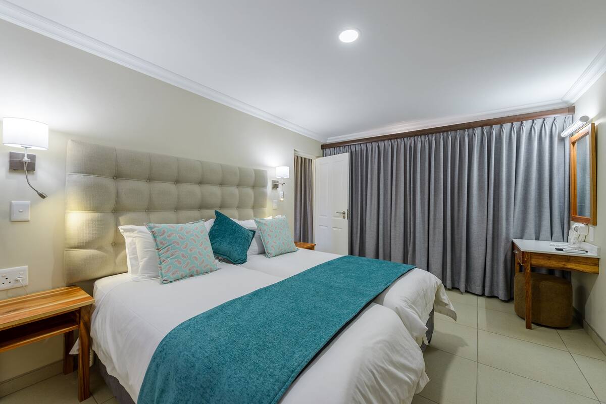 A hotel room with a large bed, a bedside table, a desk, and a mirror.