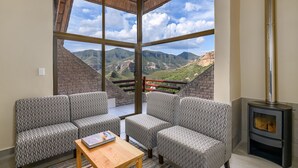 Una sala de estar acogedora con sofás estampados, una mesa de centro de madera y un amplio ventanal con vistas a la montaña.