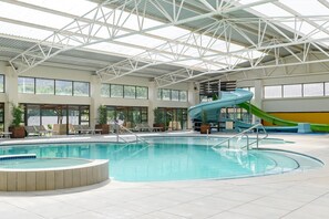 Une piscine intérieure dotée d’un toboggan, de chaises longues et d’un haut plafond avec une structure métallique.
