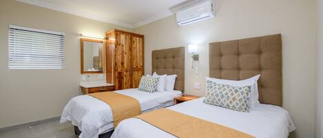 A hotel room with two beds, a wooden wardrobe, a mirror, and an air conditioning unit.
