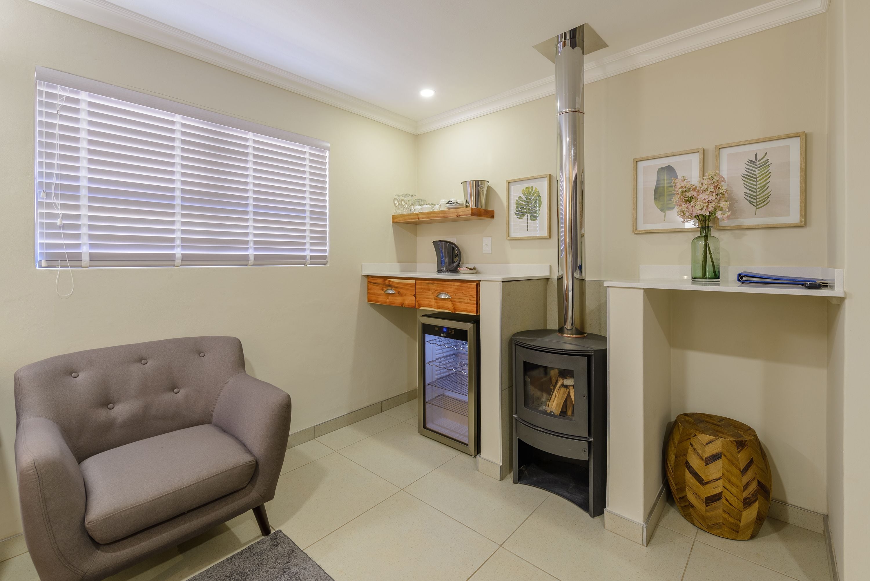 A compact living space with a sofa, a small refrigerator, a wood-burning stove, and framed botanical prints on the wall.
