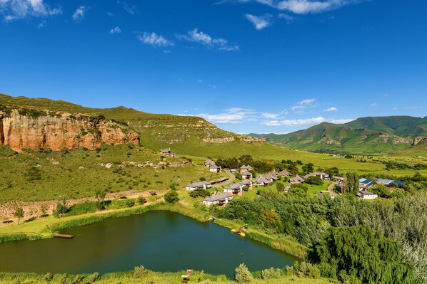 A small village with houses along a river, surrounded by green hills and a clear blue sky. - Kiara Lodge (Clarens)