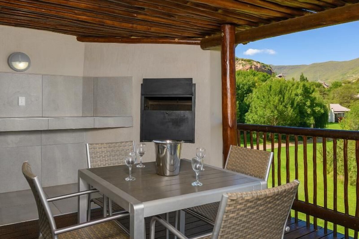 An outdoor patio with a table and chairs, a grill, and a view of the surrounding landscape.