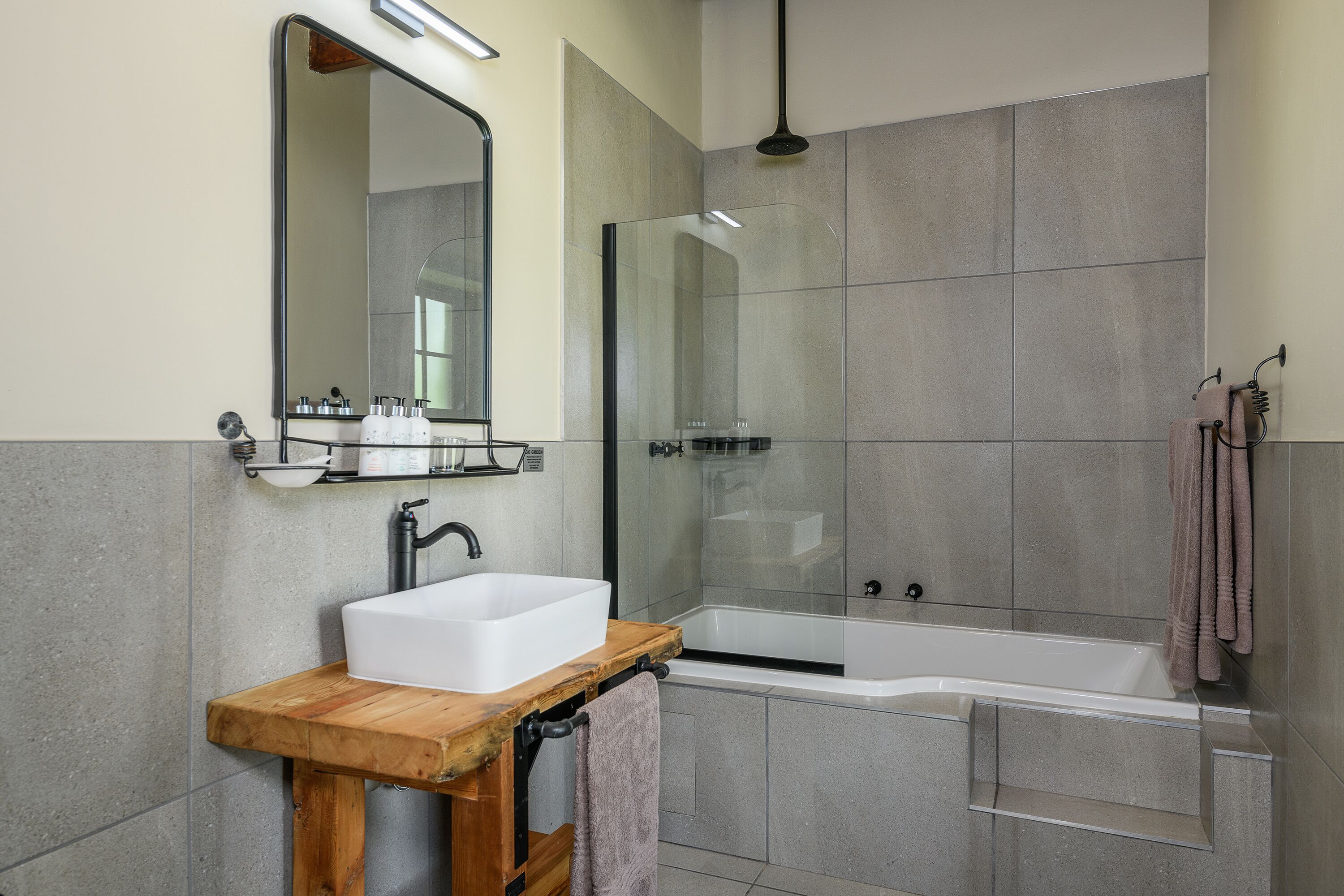 A modern bathroom with a wooden vanity, a large mirror, a bathtub, and a glass shower enclosure.