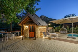 Une terrasse en bois avec un bâtiment en pierre, une piscine et des chaises longues.