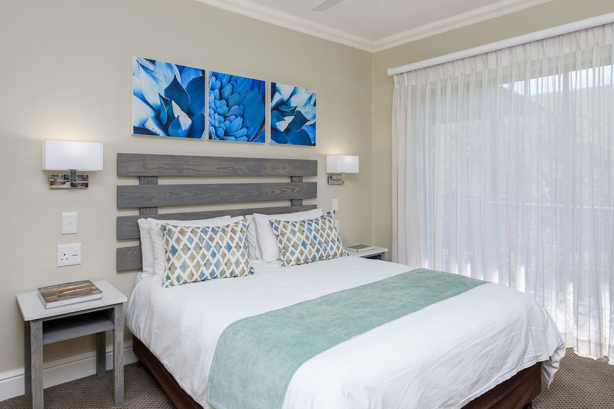 A hotel room with a bed, a nightstand, a ceiling fan, and artwork on the wall.