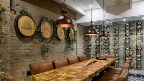 Un restaurante con una larga mesa de madera, asientos tipo banqueta de cuero y una pared de ladrillo con estanterías para vino.