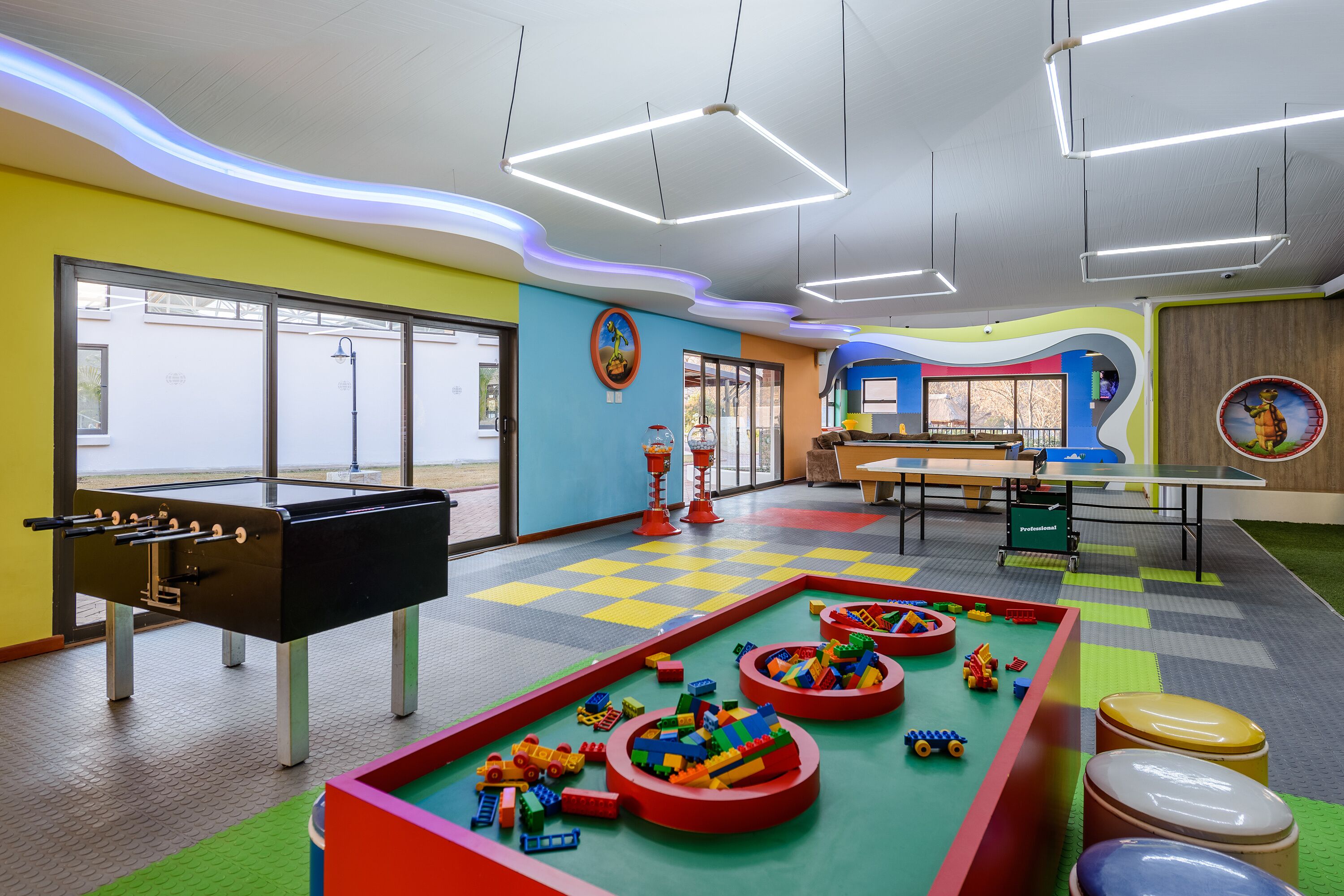 Un área de juegos interior, llena de color, con una mesa de fútbol de mesa, alfombras de juego y varios juguetes.