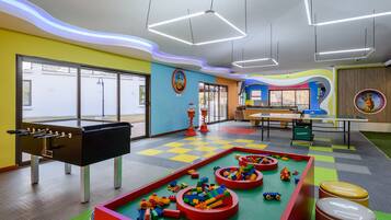 A brightly colored indoor play area with a foosball table, play mats, and various toys.