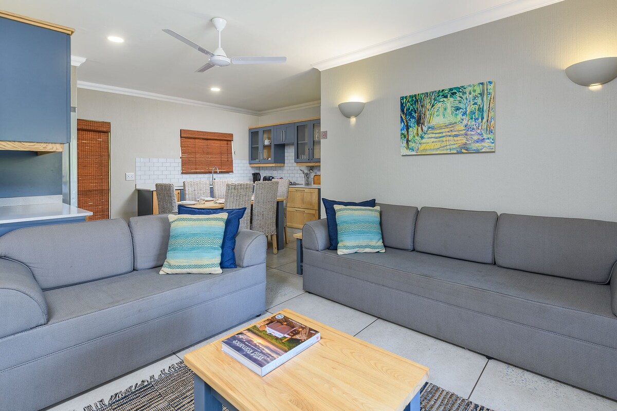 A modern living room with a grey sofa, a wooden coffee table, and a ceiling fan.