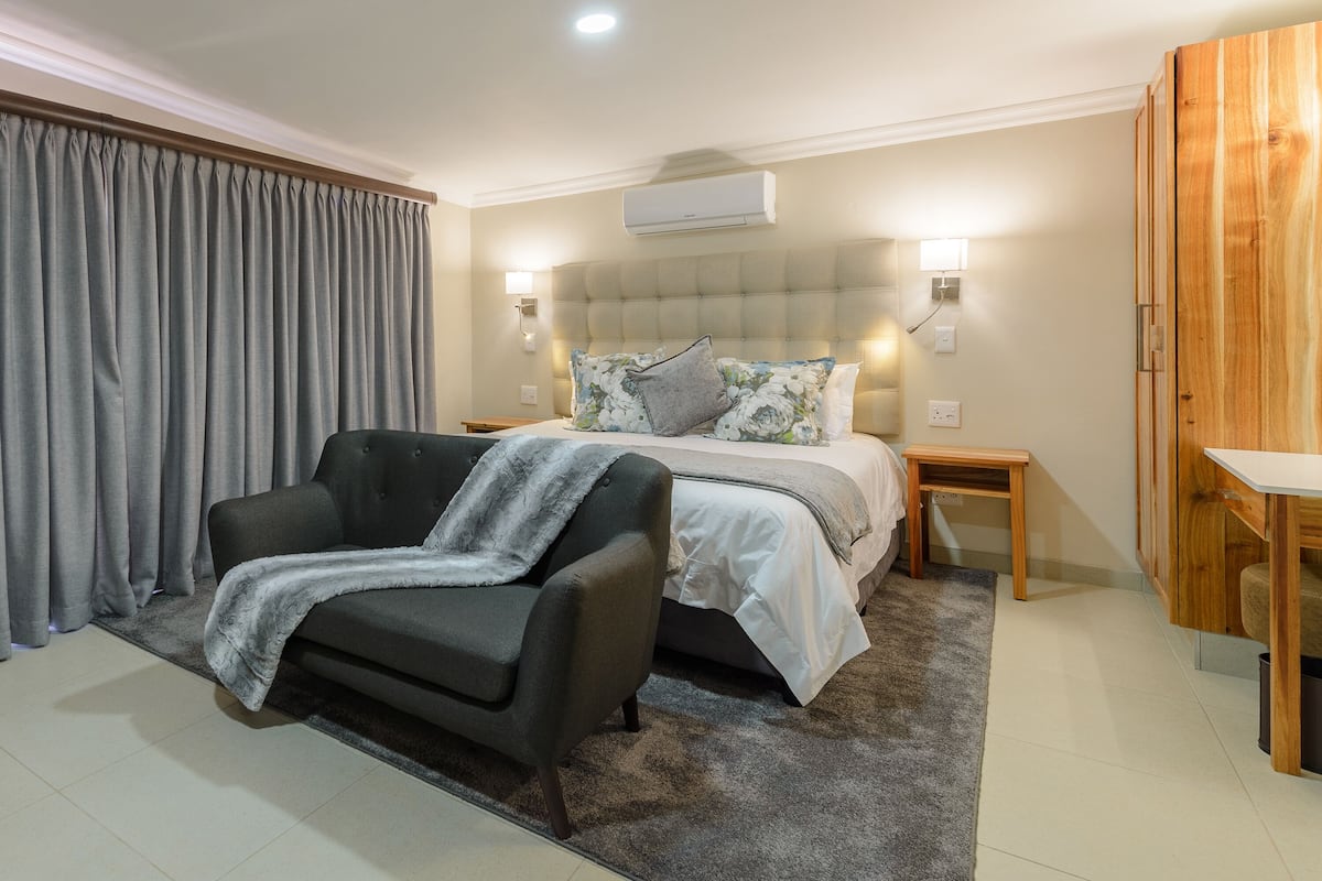 A modern hotel room with a bed, a sofa, a wooden table, and a grey curtain.