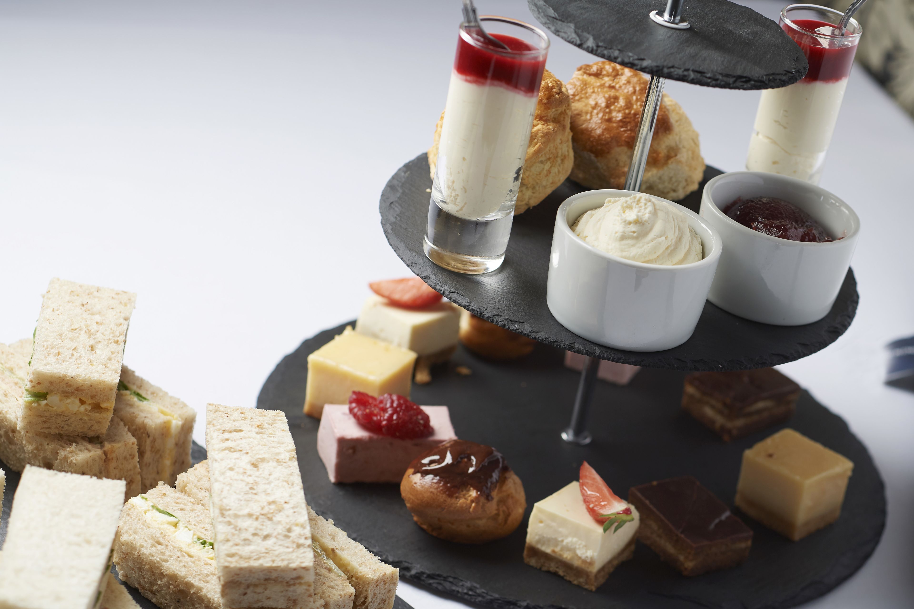 A multi-tiered dessert stand with various pastries and desserts, including scones, sandwiches, and small bowls of cream and jam.