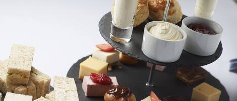 Un présentoir à étages garni de diverses pâtisseries et de desserts, notamment des scones, des sandwichs et de petits bols de crème et de confiture.