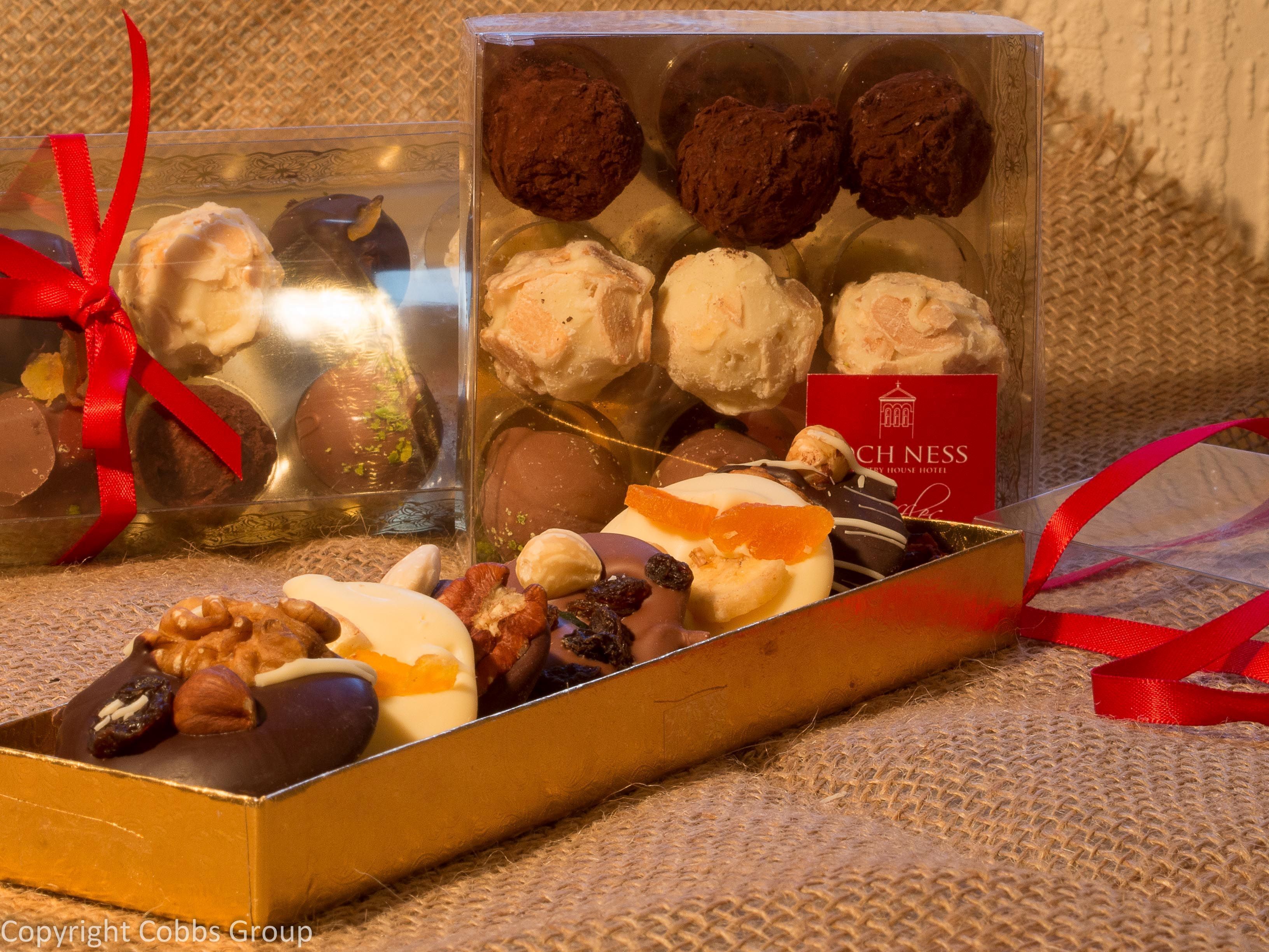 Variedad de chocolates y pasteles en una caja de regalo con lazo rojo, sobre una superficie texturizada.