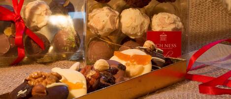 A variety of chocolates and pastries in a gift box with a red ribbon, placed on a textured surface.