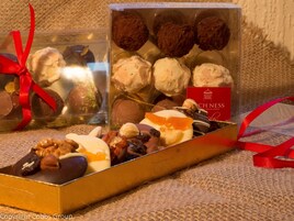 Variedad de chocolates y pasteles en una caja de regalo con lazo rojo, sobre una superficie texturizada.