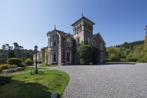 A large, historic stone building with a prominent tower and a curved wing, surrounded by well-maintained gardens and a gravel driveway. - Loch Ness Country House Hotel (Inverness)