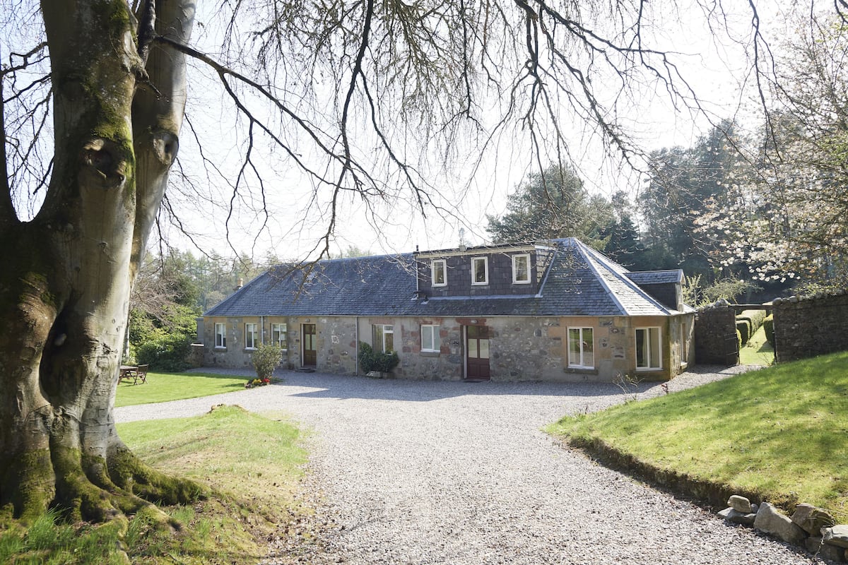 A stone building with a gravel driveway, surrounded by trees and a grassy area.