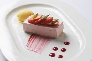 Postre sobre un plato blanco con fresas y salsa roja.